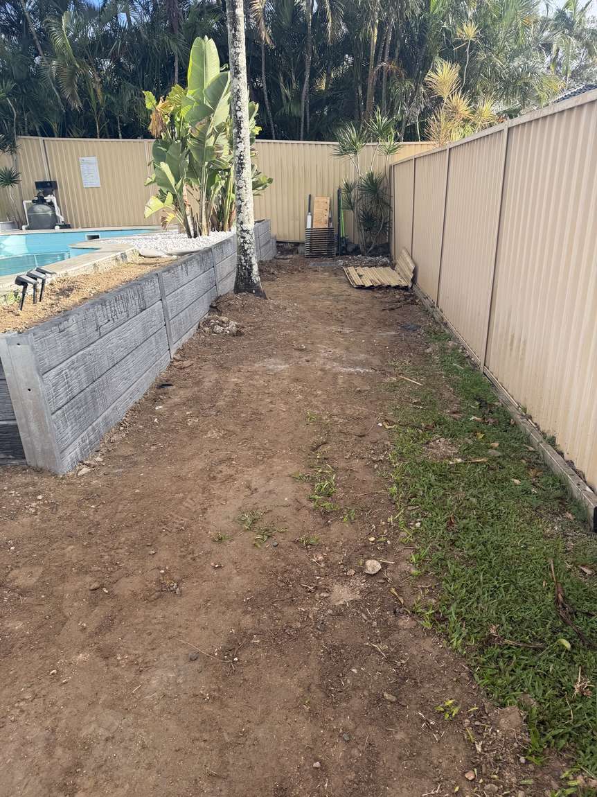 The side yard before work: rough, uneven, overgrown ground beside a pool