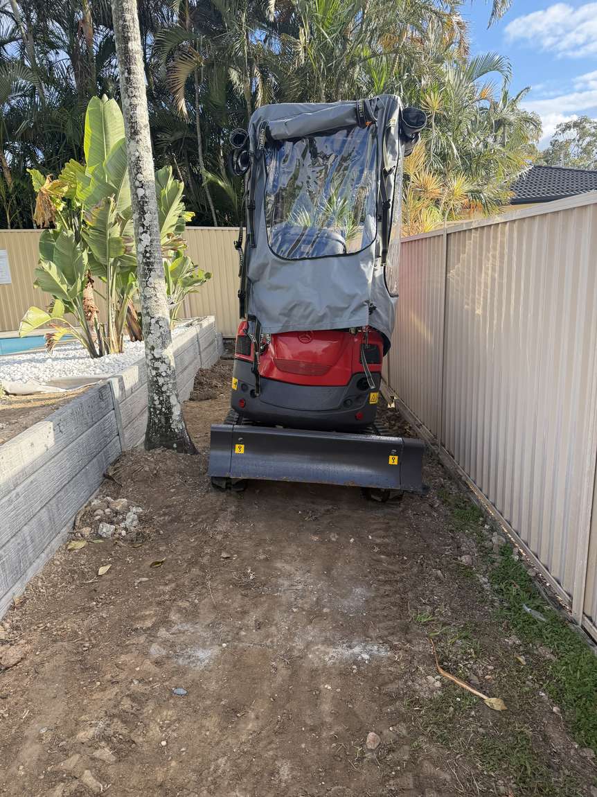 The excavator working in a narrow corridor between a house wall and a fence